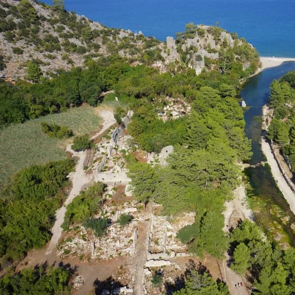 Ruins of ancient Olympos emerging from dense vegetation near the Mediterranean shore